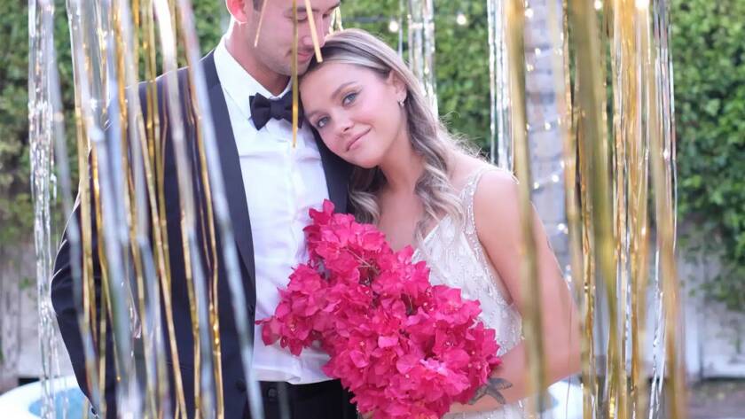 Couple with fuscia flower bouquet lean against eachother