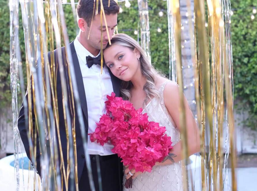Couple with fuscia flower bouquet lean against eachother
