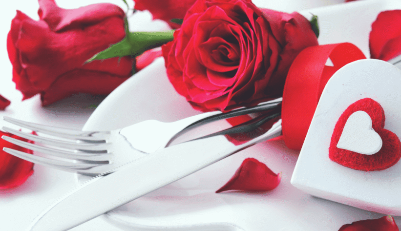white plate with fork and knife surrounded by hearts and red roses for Valentine's Day Dinner