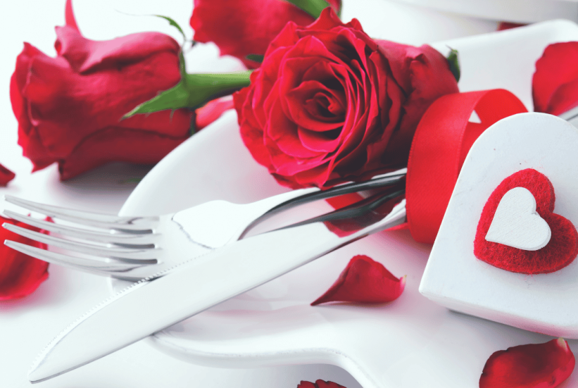 white plate with fork and knife surrounded by hearts and red roses for Valentine's Day Dinner