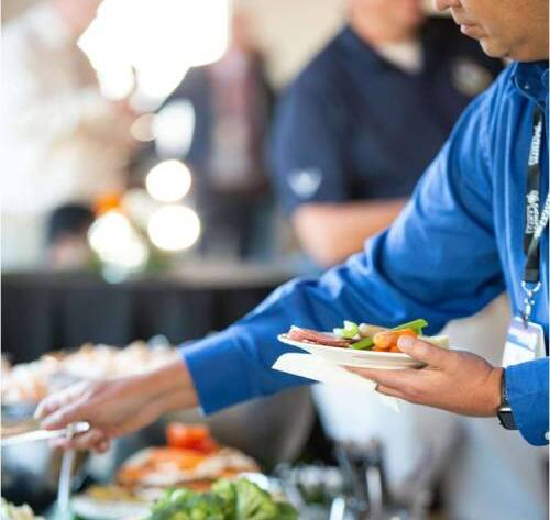 man in blue shirt selecting food from a buffet at a corporate event